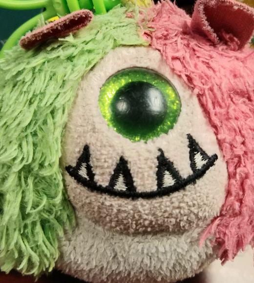 a fuzzy, round, half pink, half green, cyclops plushie with an adorable underbite