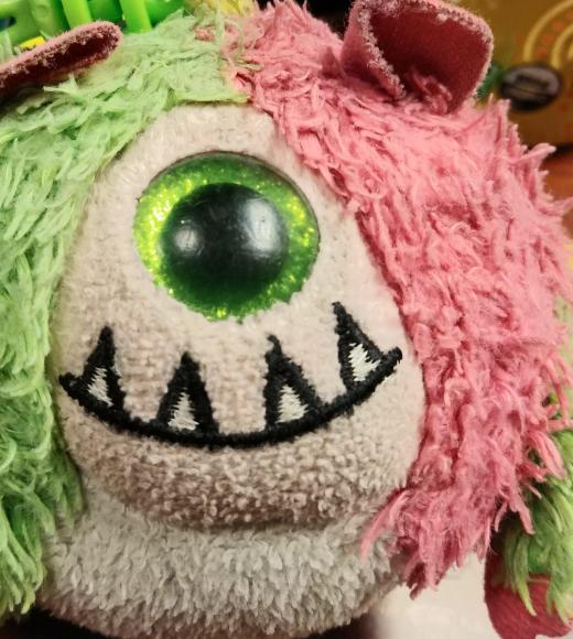 a fuzzy, round, half pink, half green, cyclops plushie with an adorable underbite